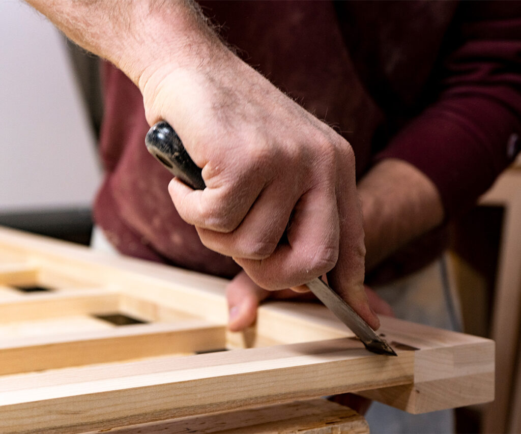 Close-up of craftsman hand-carving wood, showing how Amish furniture is made.