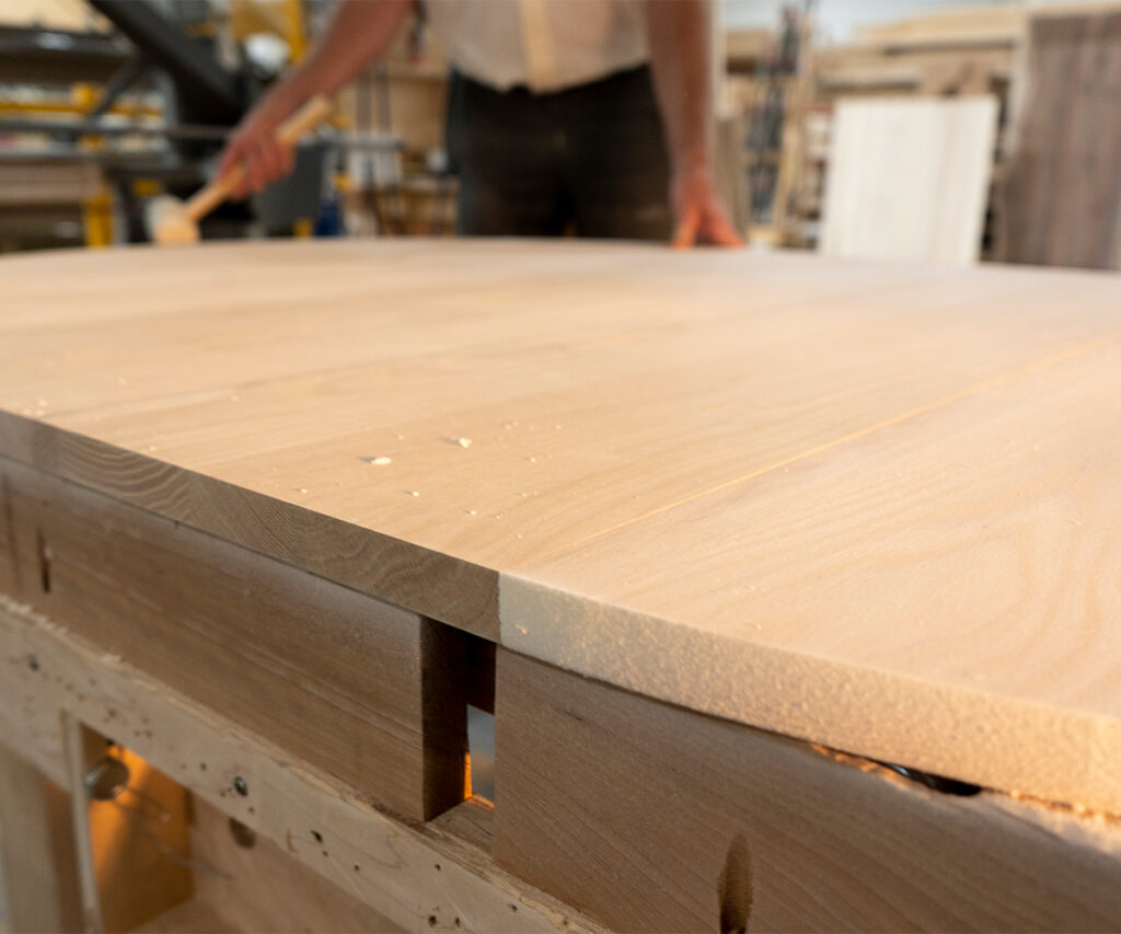 Unfinished oak tabletop showing raw grain on workbench in a woodshop.