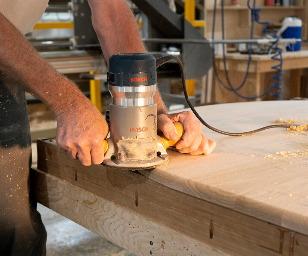 Woodworker routing oak tabletop edge with handheld Bosch router.