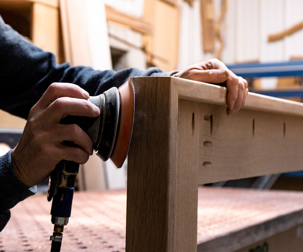 Woodworker sanding an oak bed rail to refinish and repair the surface.