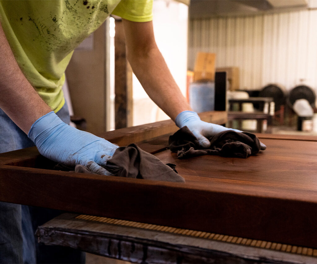 Woodworker wiping stain onto an oak panel in a workshop.